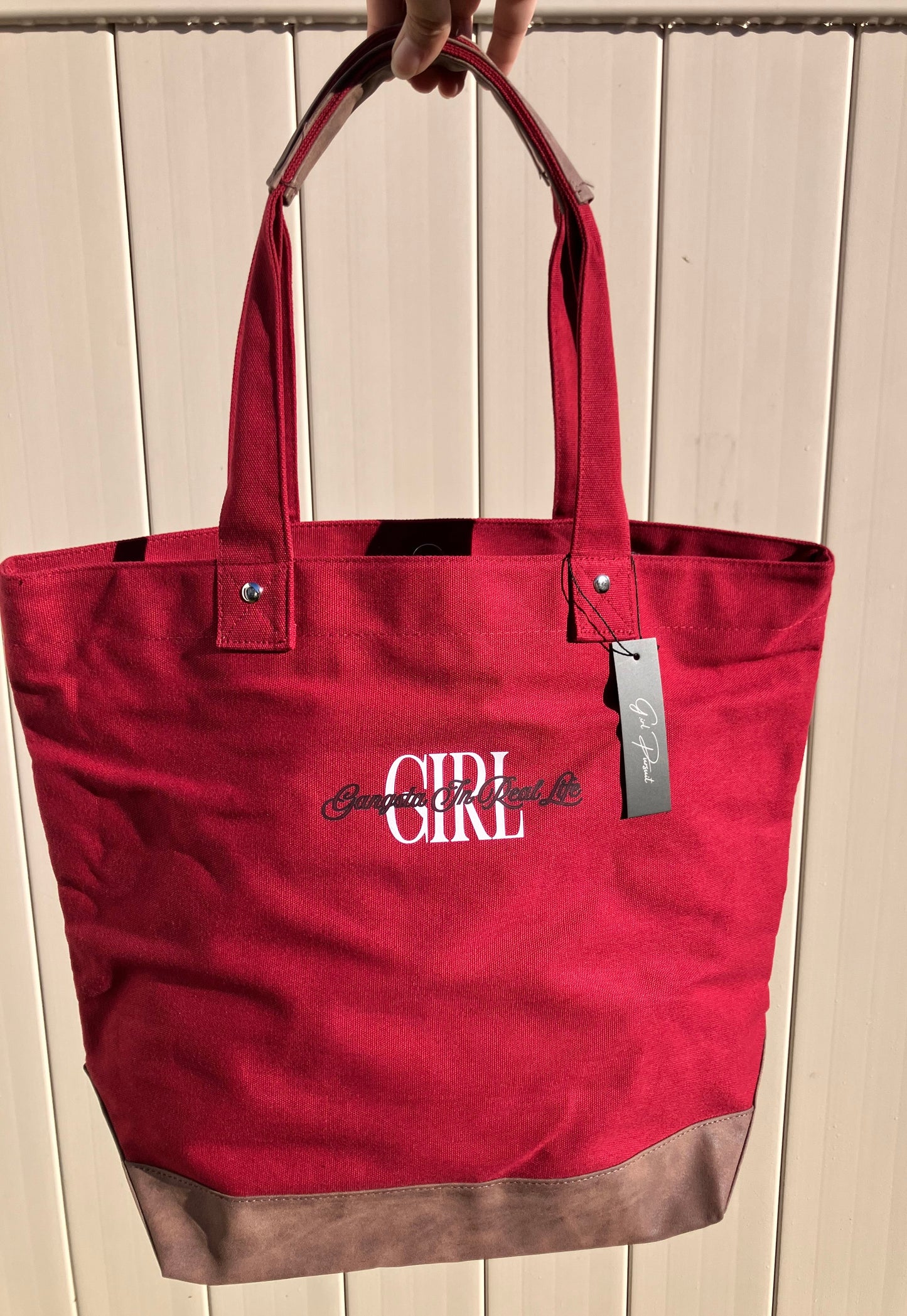 Red tote bag with Girl branding held by a hand against a wooden background