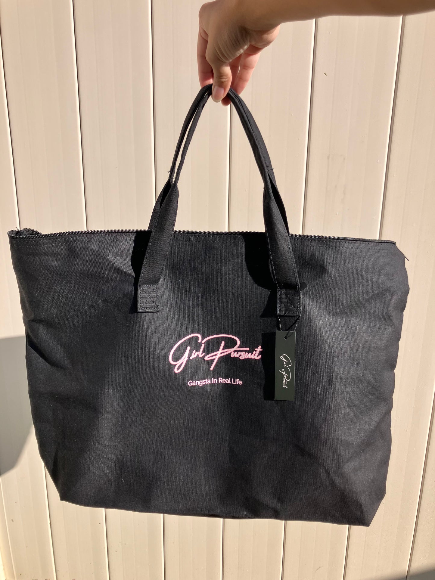 Black tote bag with a brand logo held by a hand on a light wooden surface