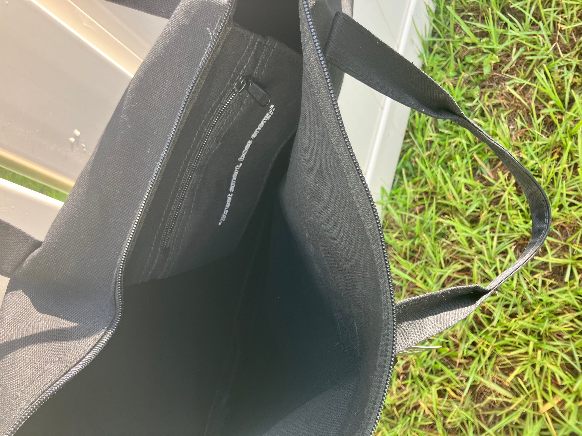 Black bag with a visible brand logo on grass and concrete surface