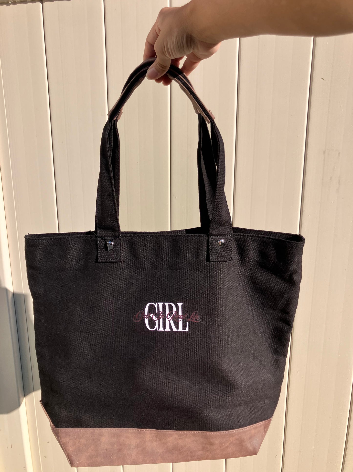 Black tote bag with 'GIRL' text held by a person against a wooden background