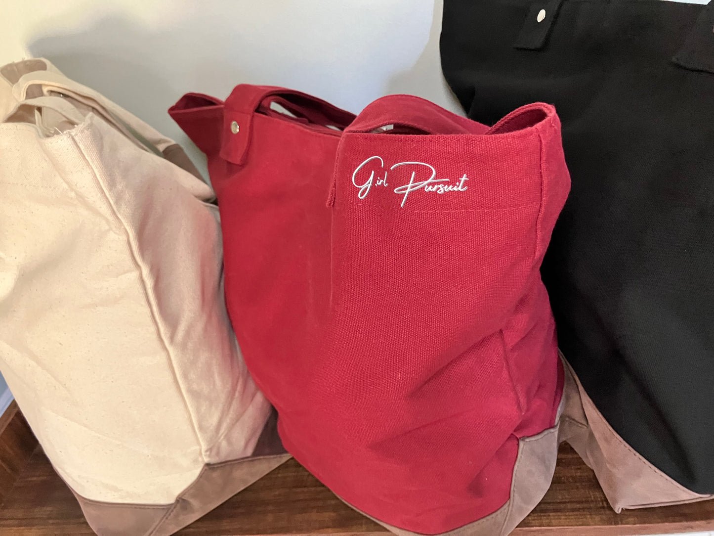 Red bag with 'Girl Pursuit' logo on a wooden surface with beige and black items.