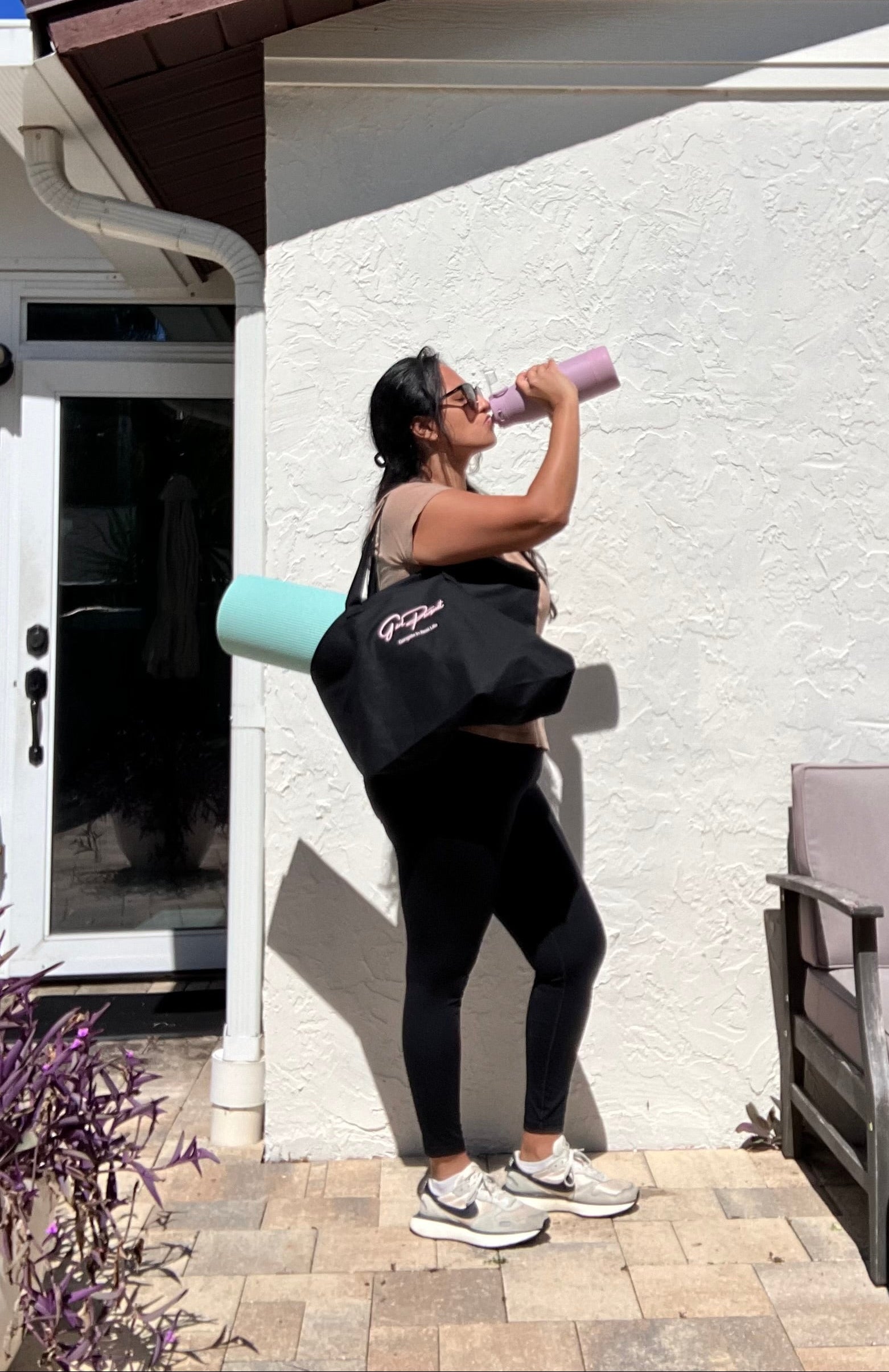 Woman exercising outdoors, holding a water bottle and a black bag with Girl Pursuit Logo and a Yoga mat in it.