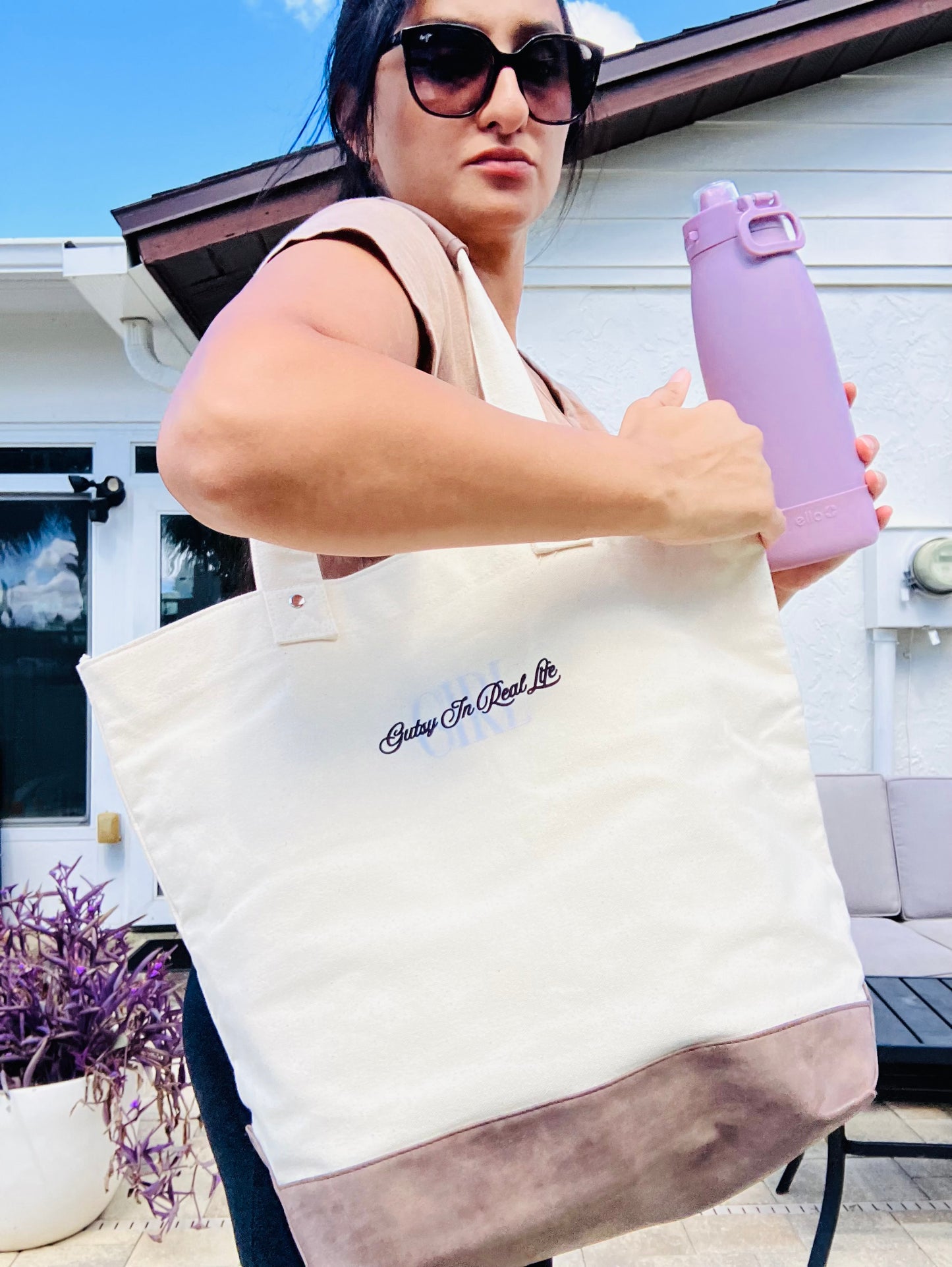 Person holding a tote bag with text and a purple water bottle outdoors.