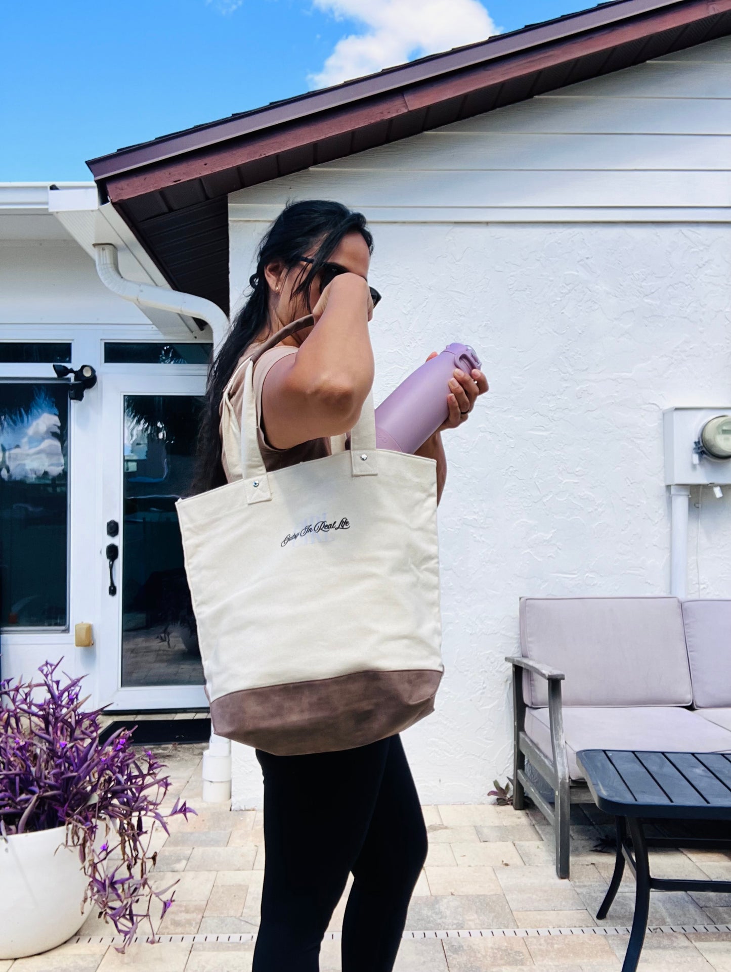 Person holding a tote bag and a pink water bottle outdoors.