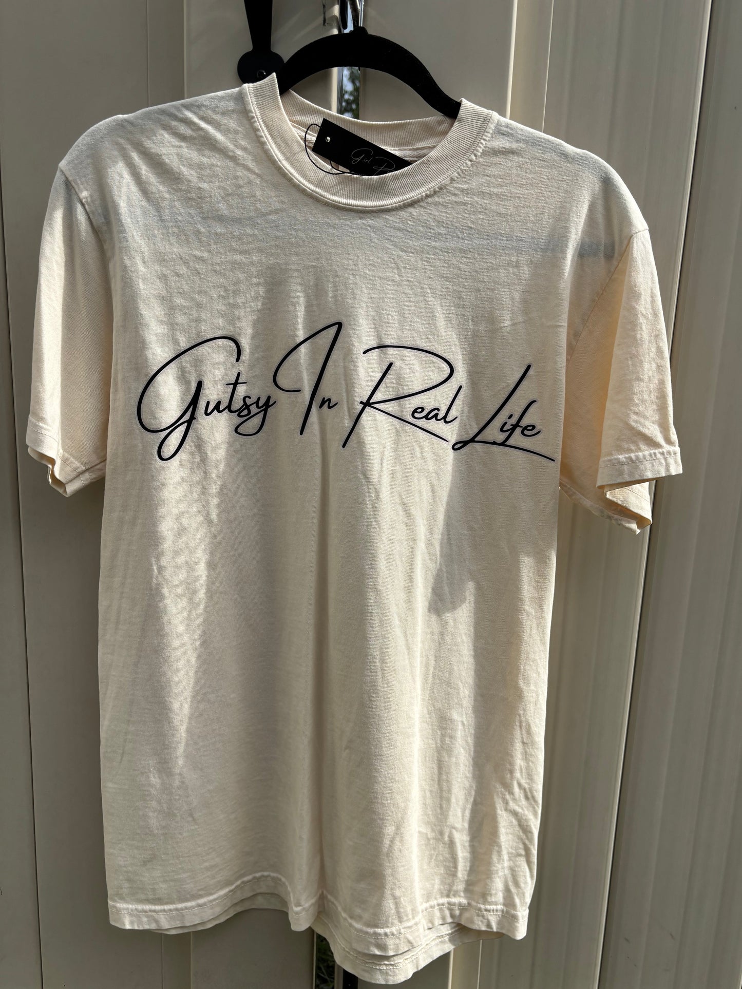 Ivory t-shirt with 'Gutsy In Real Life' text on a white surface