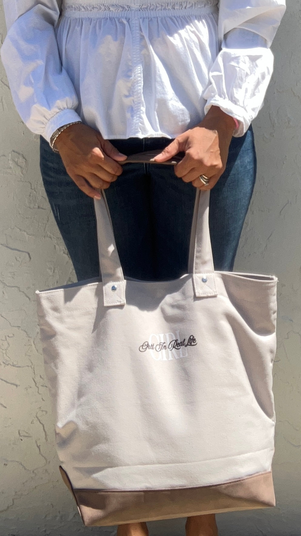 Person holding a beige tote bag with a visible brand logo against a neutral background