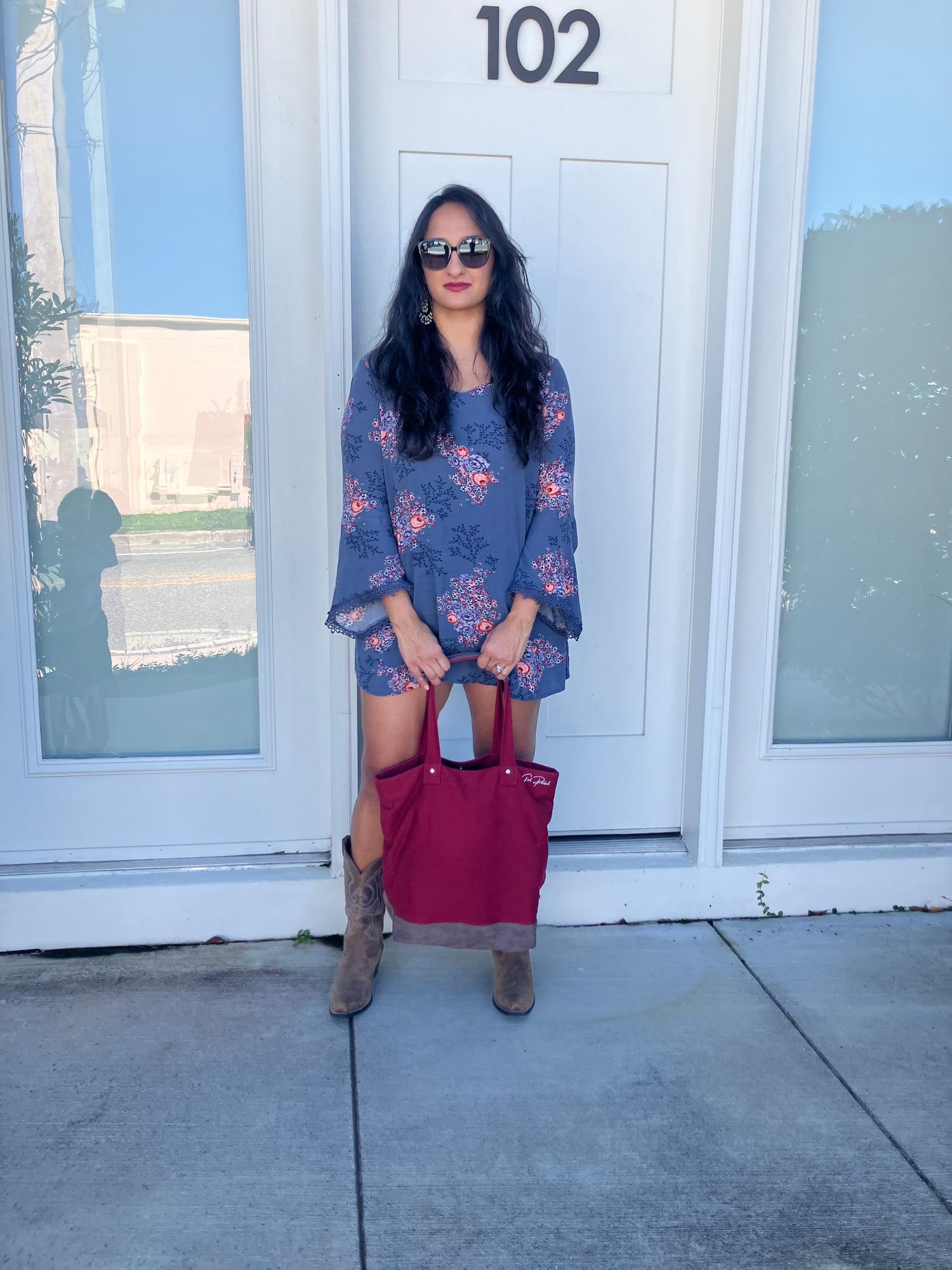 Woman standing in front of a white door with glass panels holding Girl Pursuit bag in a styled way.